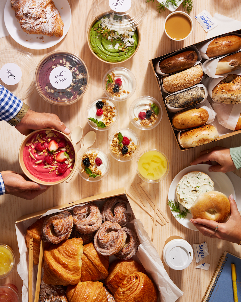 Catered breakfast spread including acai bowls, bagels, and yogurt