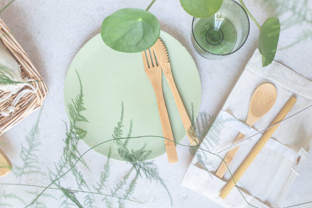 Wood cutlery on a reusable plate next to a wooden straw. 