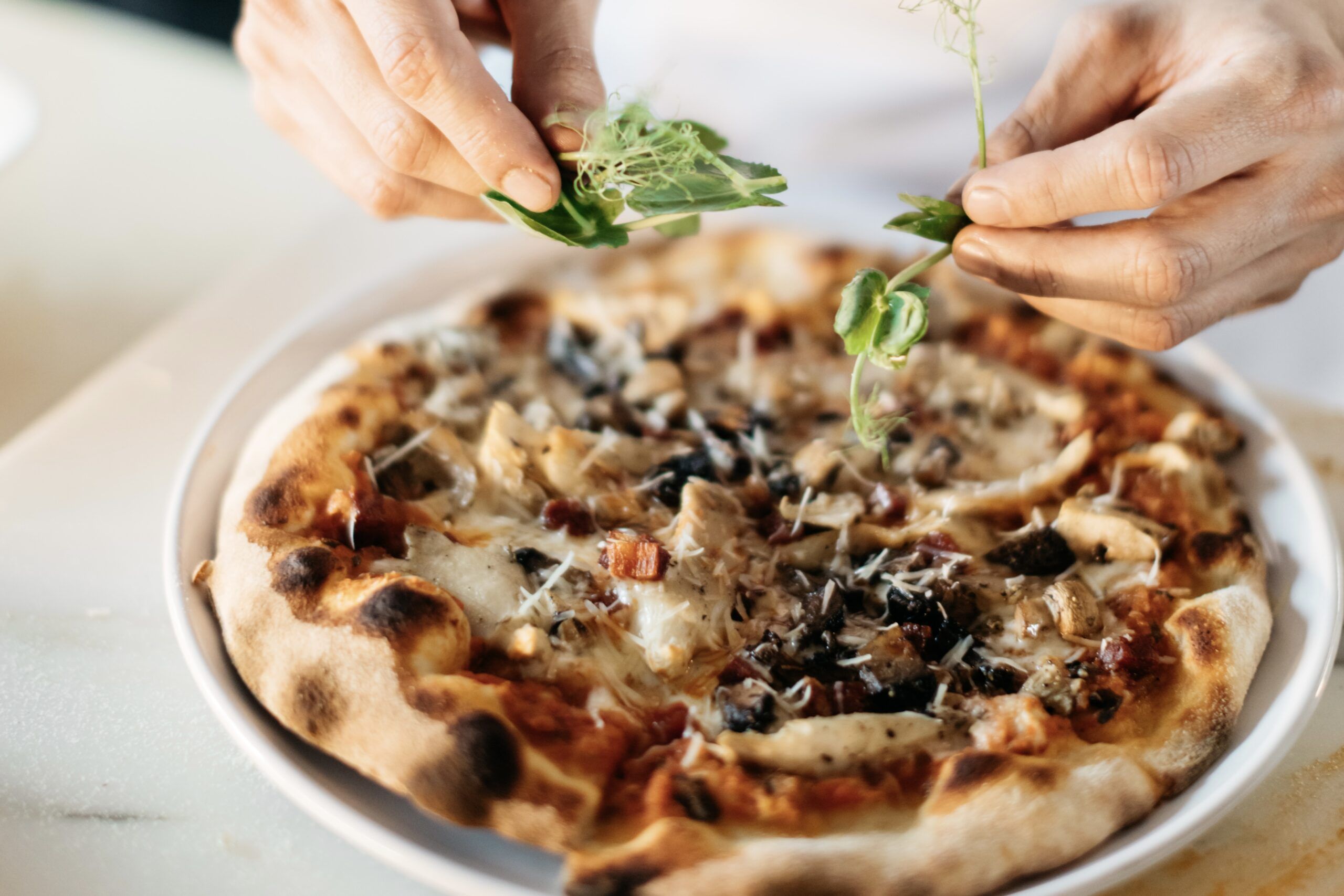 A chef placing arugula onto a pizza.