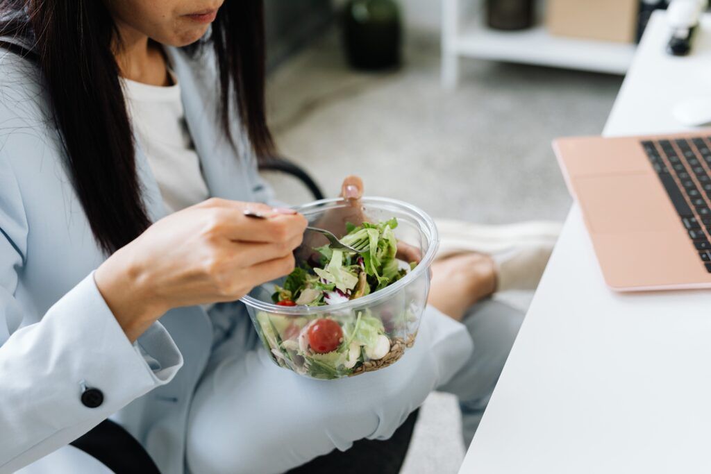 A woman eating a salad at her office desk.