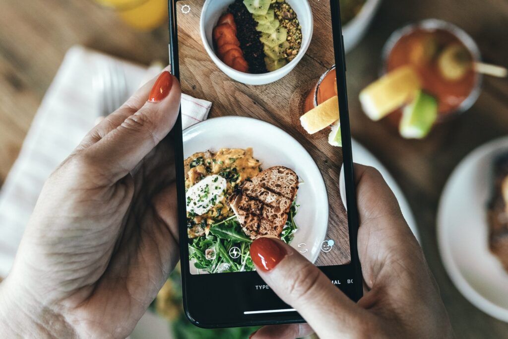 A woman taking a photo of an acai bowl and an egg dish with sourdough bread.