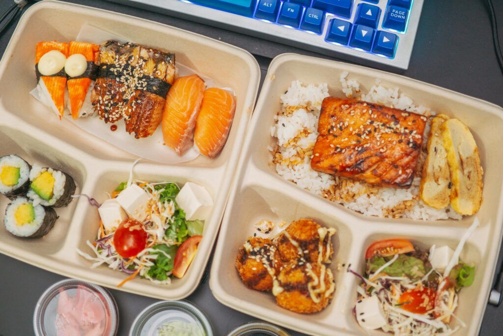 Sushi lunch in a box on a desk next to a keyboard.