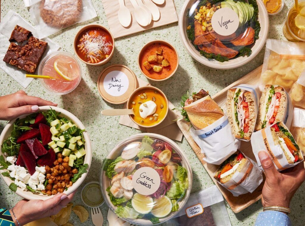 People grabbing a salad and a sandwich from a catered lunch spread. 