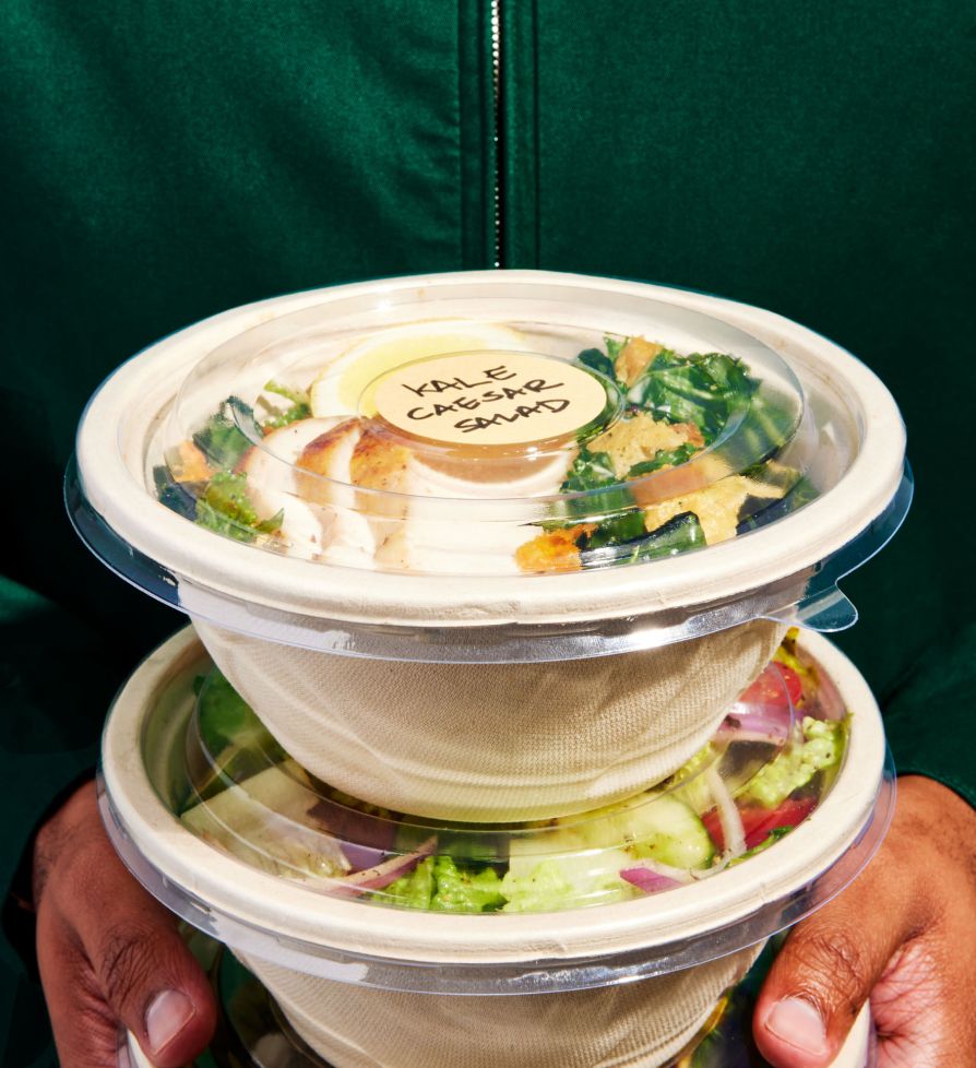 A person holding individually packaged salads, top one labeled Kale Caesar Salad
